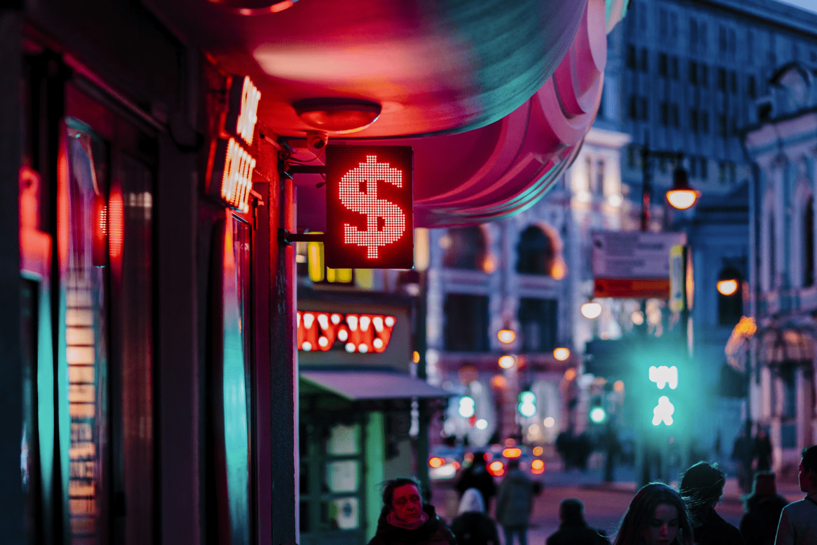 a neon dollar sign over people walking on the street during night time