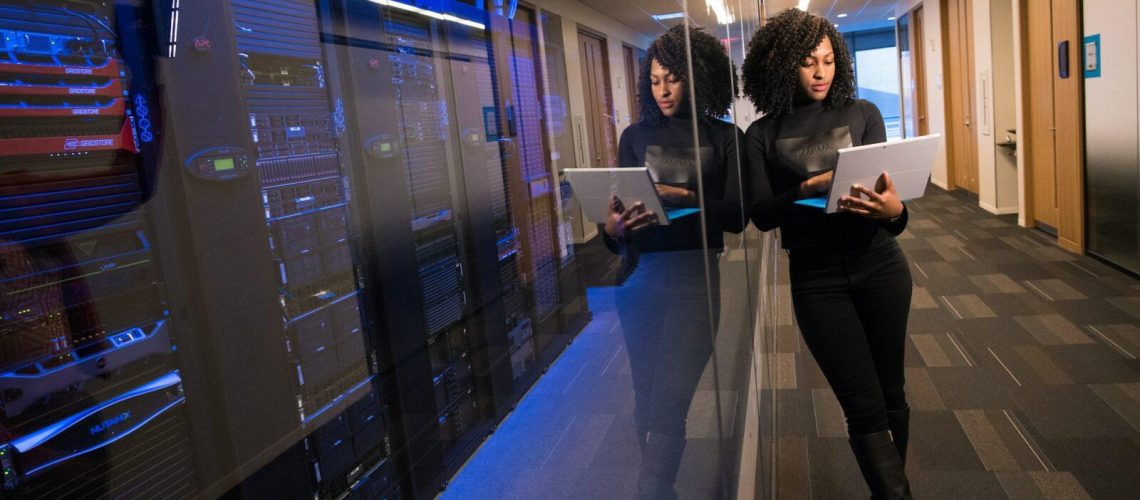 Woman Working Standing Next to Servers Holding Laptop