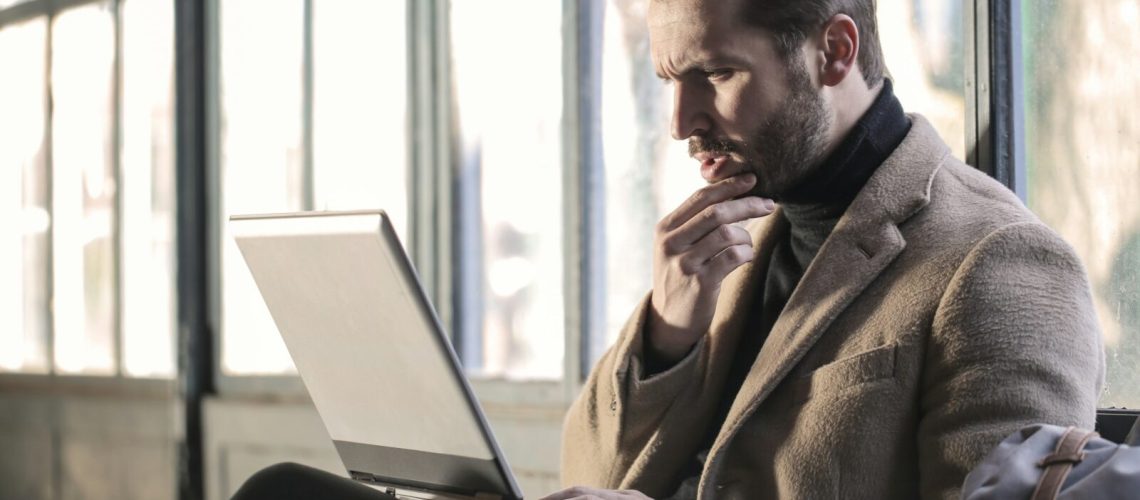 man holding his chin facing the laptop computer