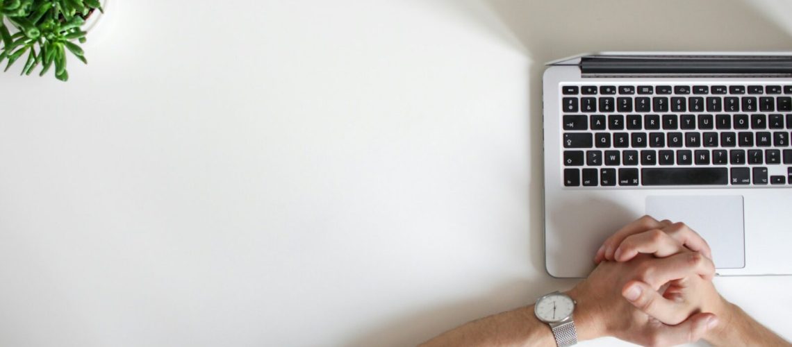 person at the office with his hands together on top of the laptop